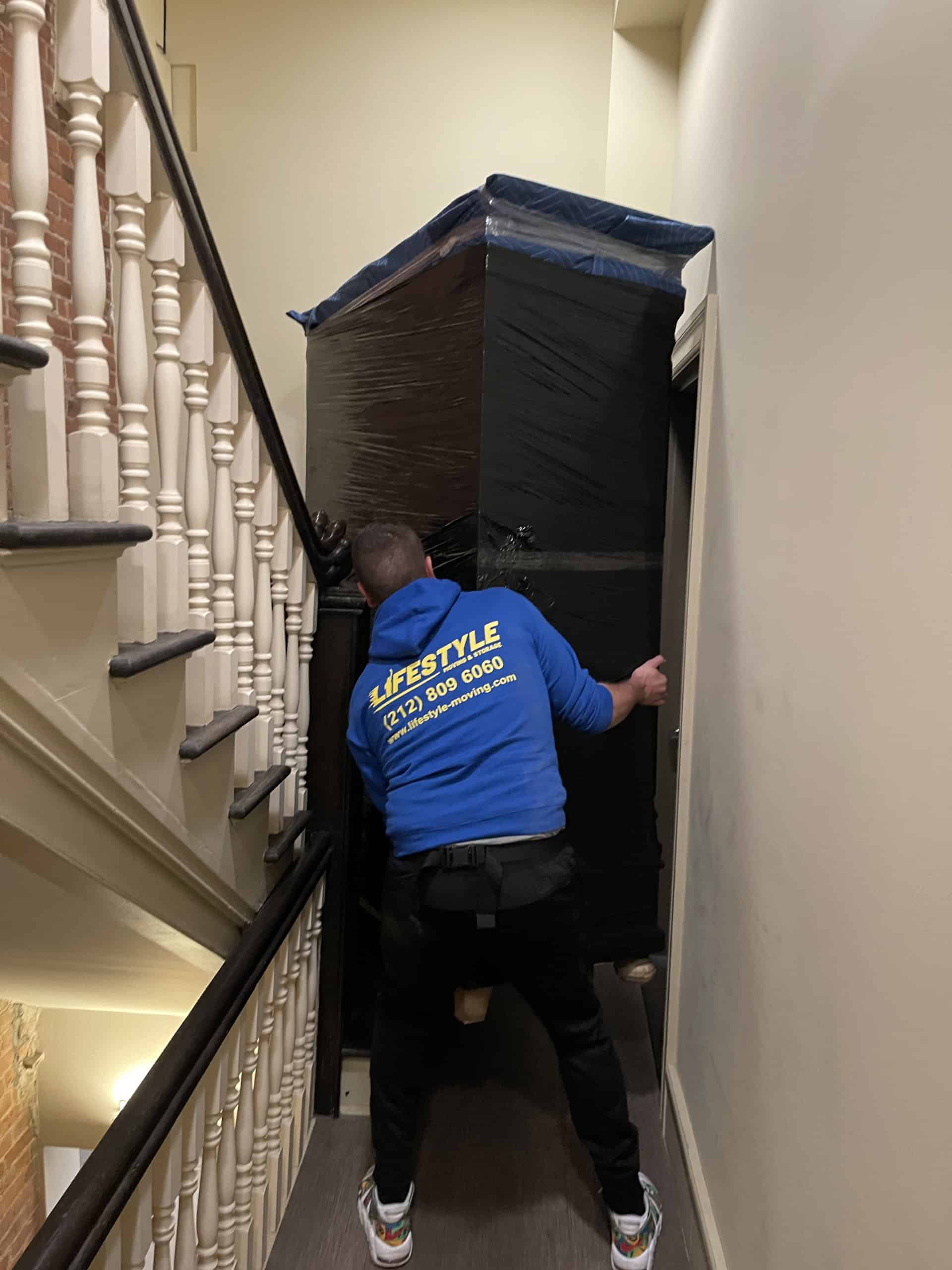 Mover carrying a wrapped item down an apartment stairway