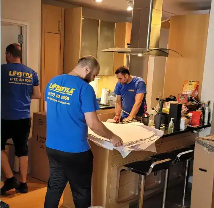 Movers packing household items in a kitchen