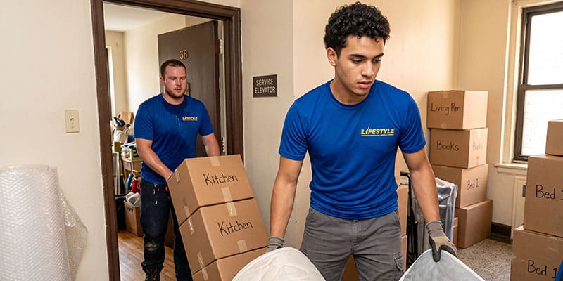 Two professional movers carrying moving boxes through a home